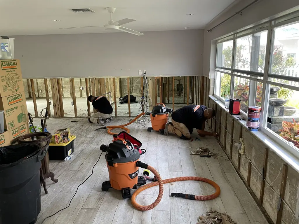Restoration crew cutting out wet drywall and running wet vacuums in a storm flooded sunroom