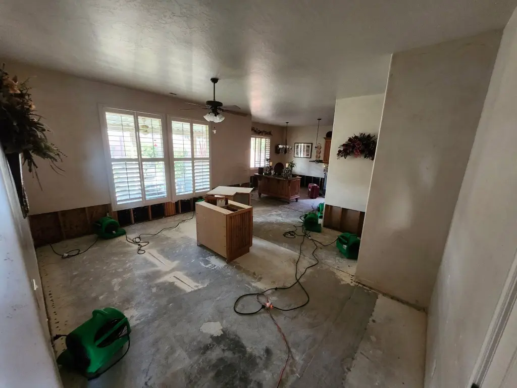 Living room after water extraction with flooring removed and air movers drying the exposed floor
