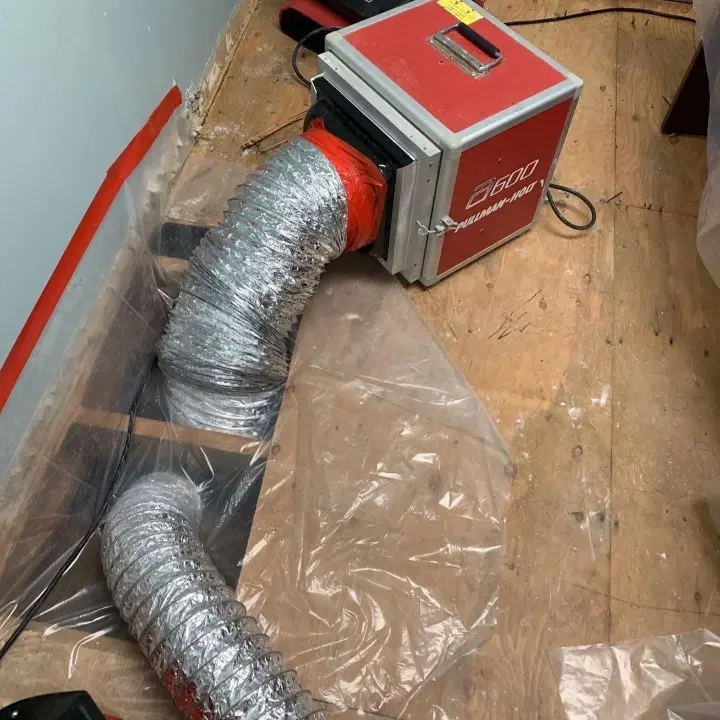 HEPA air scrubber with ducting running inside plastic containment during a sewage cleanup