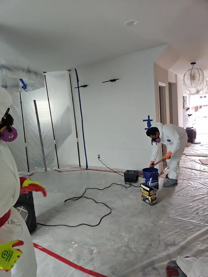 Technicians in respirators working inside plastic sheeting containment set up before mold removal